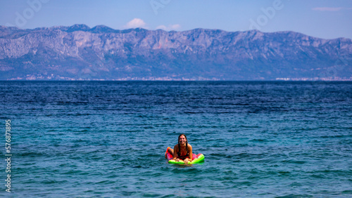 relaxed girl in a bikini floating on a strawberry shaped mattress in adriatic sea, croatia; leisure on the shore of mediterranean sea, holidays in europe