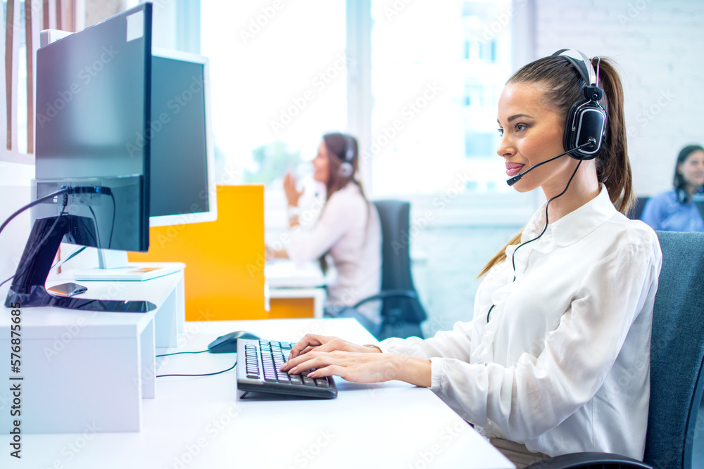IT service desk operator woman in headset working on computer at call center. IT service desk operator woman in headset working on computer at call center.