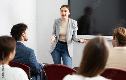 Young woman standing near interactive board and communicating with adult students during advanced training courses in classroom