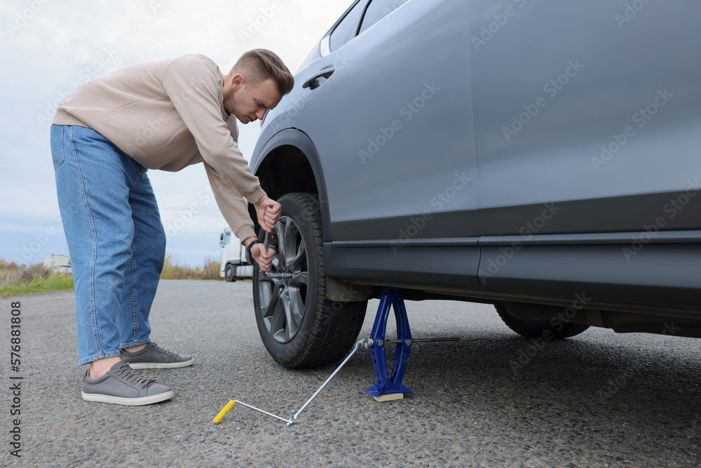 Young man changing tire of car on roadside Young man changing tire of car on roadside