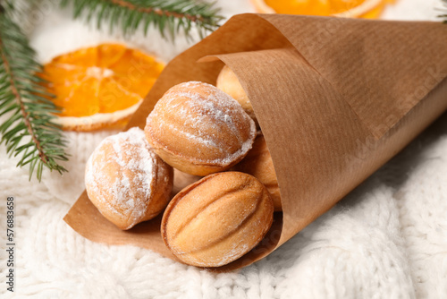 Delicious nut shaped cookies, dried orange slices and fir tree branches on white knitted fabric, closeup