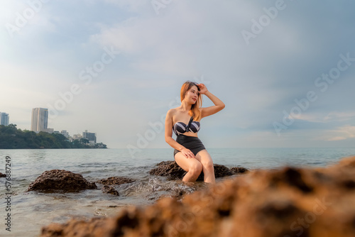 Sexy asian woman Wear a black body suit. Sitting on a rock in the sea