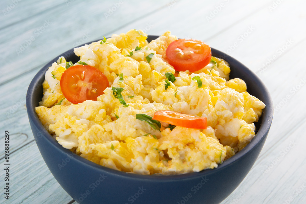Scrambled eggs with tomatoes on a bowl, wooden table Scrambled eggs with tomatoes on a bowl, wooden table