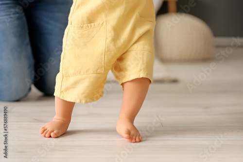 Baby boy learning to walk with his mother in bedroom, closeup
