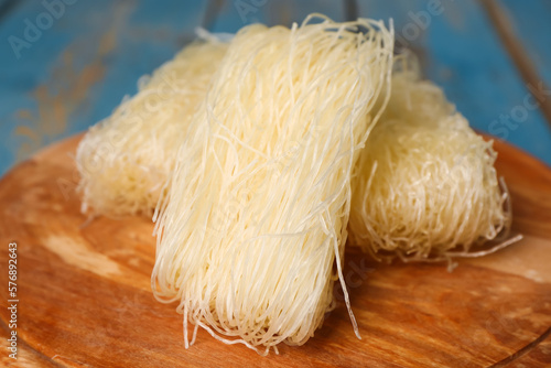 Board of raw rice noodles on color wooden background, closeup