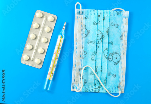 Children's medical mask, thermometer, pills on a blue paper background