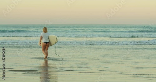 Female surfer with board enter cyan green Costa Rica waves in sunrise