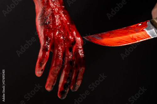 Man holding knife with bloody hand on black background. 