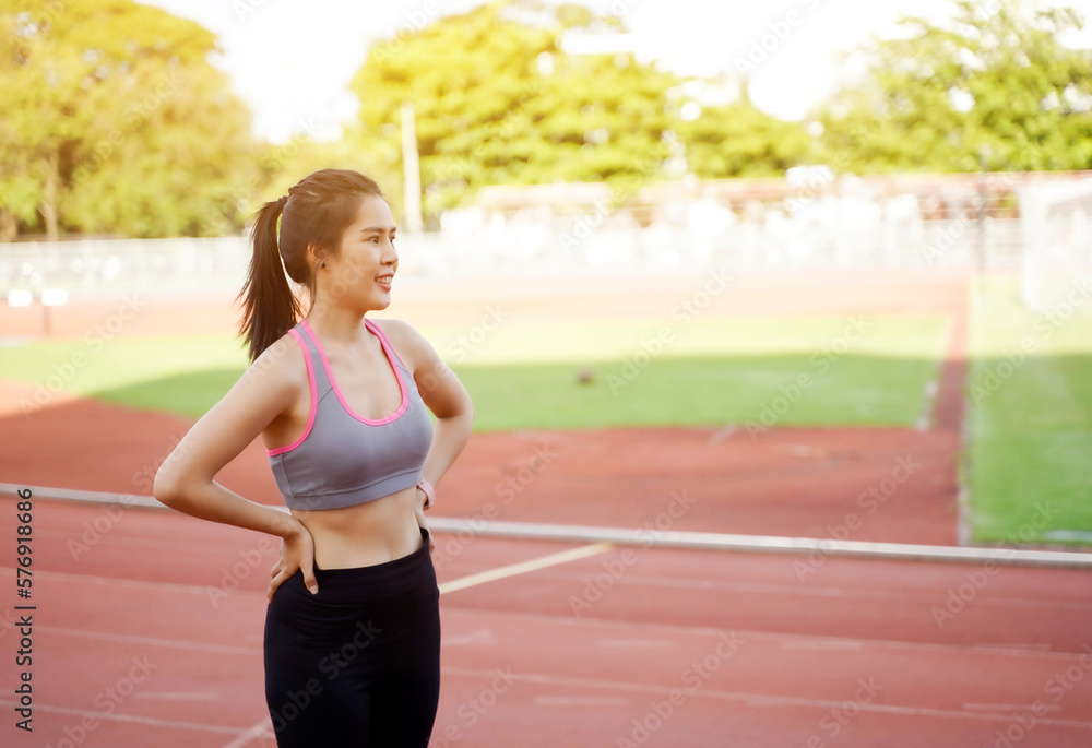 Young Asian female relaxing after workout and jogging at the football stadium in the morning with sun flare background. Young Asian female relaxing after workout and jogging at the football stadium in the morning with sun flare background.