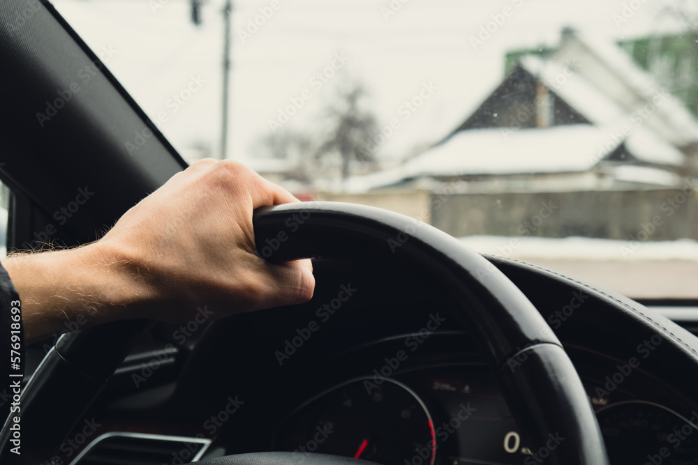 Obraz premium Selective focus man's hand on steering wheel, driving car in winter background. Black luxury modern car Interior. Steering wheel, shift lever and dashboard. Black leather Detail Automatic gear stick