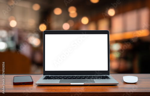Laptop with blank screen on wood table in blurry background with coffee shop or office ,nature orange bokeh and sunlight in morning.