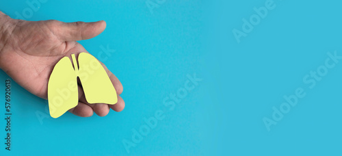 a man's hand holds a lung symbol cut out of yellow paper on a blue background, a banner, a copyspace. the concept of healthy lungs, ecology, clean air, industrial emissions reduction