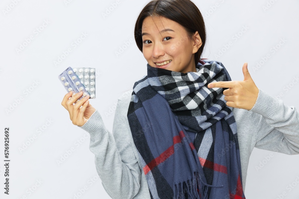 Asian woman smile cold flu holding medicine and pills in plaid with fever sick of the virus on a white background, copy space Asian woman smile cold flu holding medicine and pills in plaid with fever sick of the virus on a white background, copy space