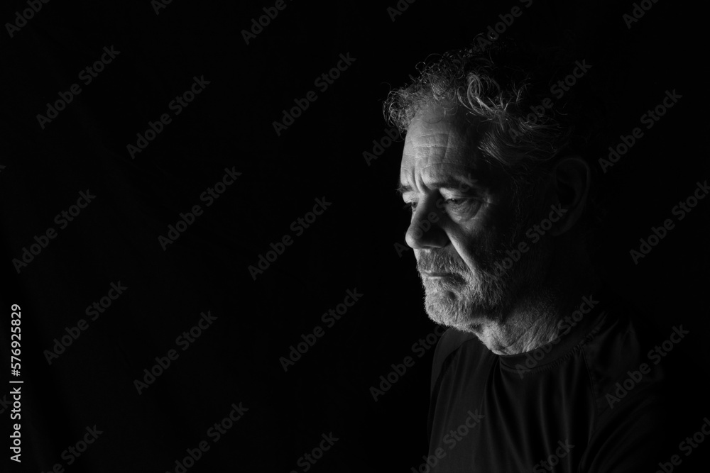 Black and white portrait of an attractive older Caucasian man with grey hair and beard. Turned to the right side, looking downward, with a thoughtful or pensive expression.  Room for copy.