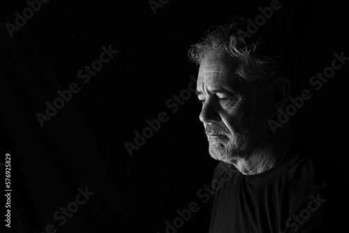 Black and white portrait of an attractive older Caucasian man with grey hair and beard. Turned to the right side, looking downward, with a thoughtful or pensive expression. Room for copy.
