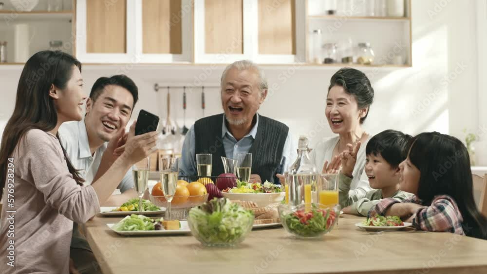 happy three generational asian family sitting at dining table at home enjoying meal together happy three generational asian family sitting at dining table at home enjoying meal together