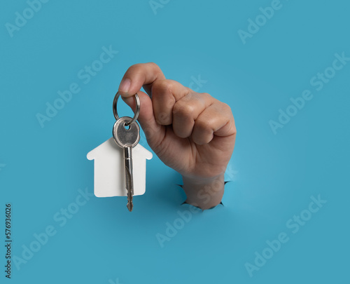 Female hand holding house key breaks through blue paper background.