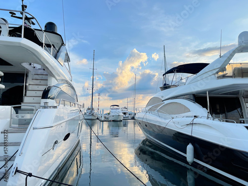 Luxury yacht in marina. Space between two yachts. Boards of yachts in the foreground. Moored sailboats in the distance on the horizon. Beautiful sunset in the sea lagoon. Expensive vessels. Photo