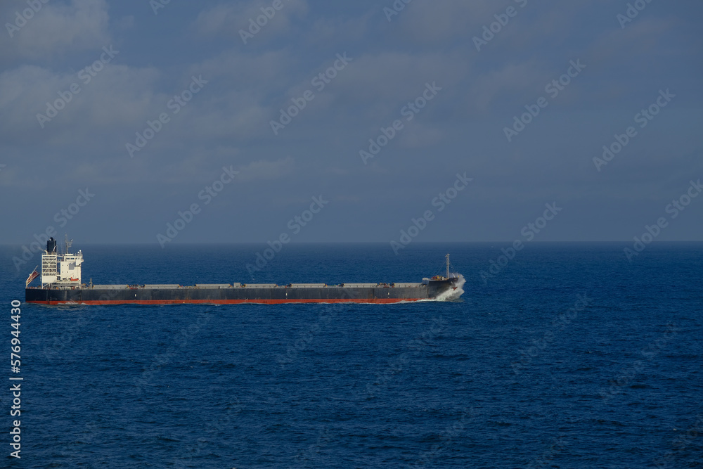 Container bunker cargo ship at sea with high swell and spray on bow while sailing at high sea ocean on sunny day with dramatic cloudscape