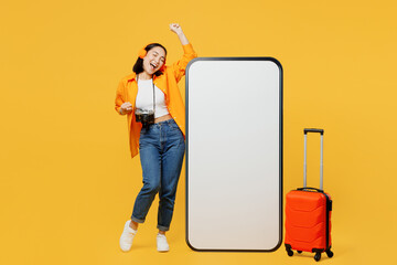 Young woman wear summer clothes big blank screen mobile cell phone listen music isolated on plain yellow background. Tourist travel abroad in free time rest getaway. Air flight trip journey concept.