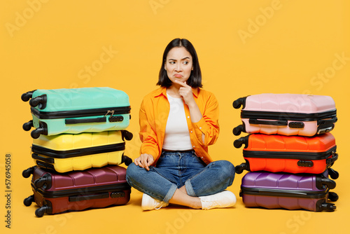 Young sad woman in summer casual clothes sit near stack of bags prop up chin isolated on plain yellow background Tourist travel abroad in free spare time rest getaway Air flight trip journey concept. photo