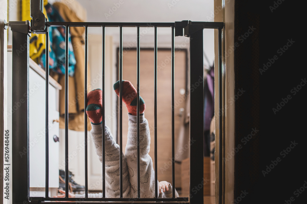 Front view of a little boy standing on the other side of the child safety gate. A little boy is holding on to the top of the security gate and looking at the camera from above. Front view of a little boy standing on the other side of the child safety gate. A little boy is holding on to the top of the security gate and looking at the camera from above.