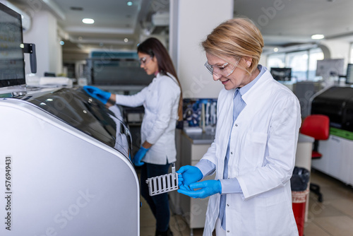 Female Research Scientist Putting Test Tubes with Blood Samples into Analyzer Medical Machine. Scientist Works with Modern Medical Equipment in Pharmaceutical Laboratory.