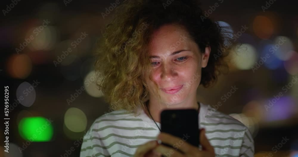 Woman on background of night cityscape books plane ticket online using phone. A caucasian woman arranges the purchase of tickets online while standing on balcony at night. A woman buys tickets online. Woman on background of night cityscape books plane ticket online using phone. A caucasian woman arranges the purchase of tickets online while standing on balcony at night. A woman buys tickets online.