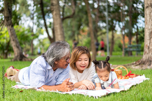 Portrait of happy love asian grandfather with grandmother and asian little cute girl enjoy relax in summer park.Young girl with their laughing grandparents smiling together.Family and togetherness