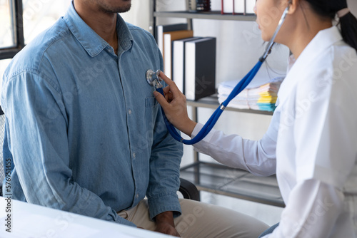 An Asian female doctor uses a stethoscope to listen to the heartbeat of a male patient for guidance in treatment and preventive care. health check concept. photo