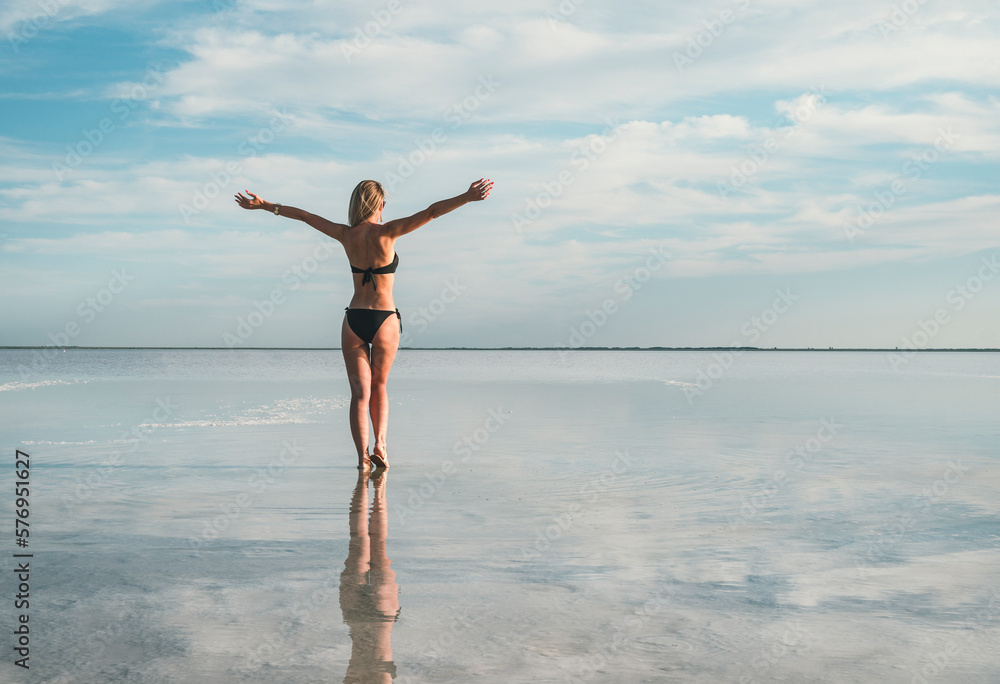 concept of freedom of travel and independence. Beautiful young girl bathes in a lake. silhouette of slender body is reflected in water. hair is loose, arms are spread out to sides. Sky with cloud