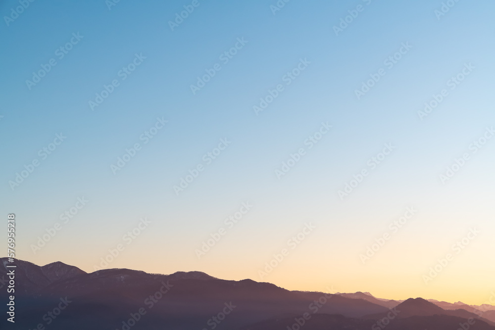 Hazy misty burgundy mountain silhouettes with aerial perspective against a sundown sky. Soft blue and yellow gradient Hazy misty burgundy mountain silhouettes with aerial perspective against a sundown sky. Soft blue and yellow gradient