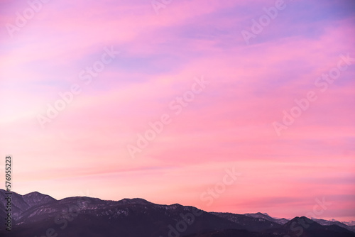 Gentle sky gradient from the setting sun over the dark silhouette of the mountains. Feeling of spring. Blue, pink, orange tones.