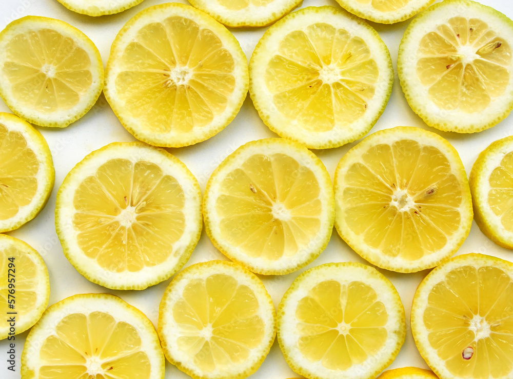 Lemons slices on white background closeup. Top view. Vibrant abstract pattern of juicy pieces, which bright circles look like small suns. Fresh healthy food, tasty fruit from Greek garden.