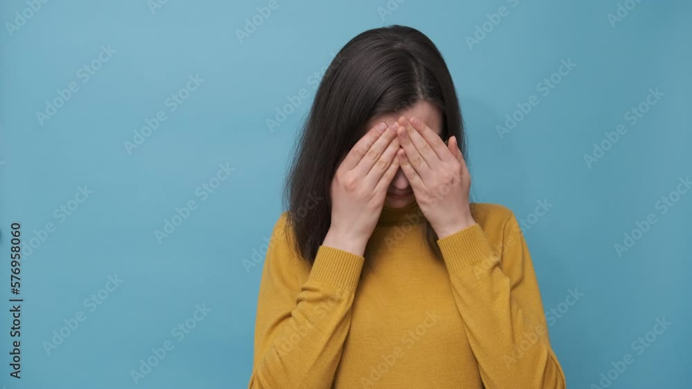 A frustrated female student in glasses and a sweater covering her eyes with her hands on a blue background, 4K. The girl is worried about her studies, love, relationships A frustrated female student in glasses and a sweater covering her eyes with her hands on a blue background, 4K. The girl is worried about her studies, love, relationships
