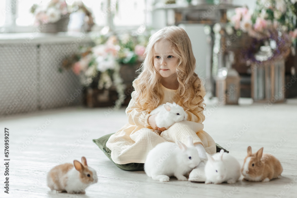 A little smiling girl in a yellow dress is playing on the floor in a room with rabbits. A baby and a rabbit. The living room is decorated for Easter. A little smiling girl in a yellow dress is playing on the floor in a room with rabbits. A baby and a rabbit. The living room is decorated for Easter.