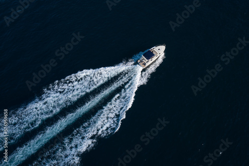 A white boat with a blue awning moving fast diagonally on dark blue water, top view. © Berg