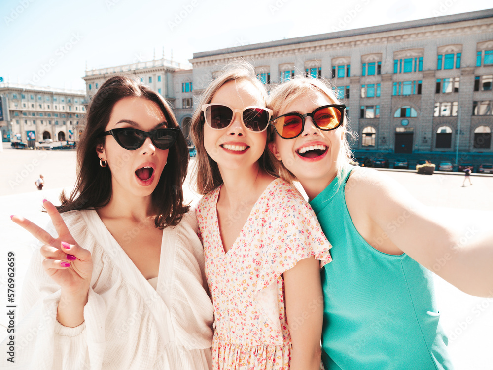 Three young beautiful smiling hipster female in trendy summer dresses clothes. Sexy carefree women posing in the street. Positive models having fun, talking, chatting. In sunglasses. Taking selfie Three young beautiful smiling hipster female in trendy summer dresses clothes. Sexy carefree women posing in the street. Positive models having fun, talking, chatting. In sunglasses. Taking selfie