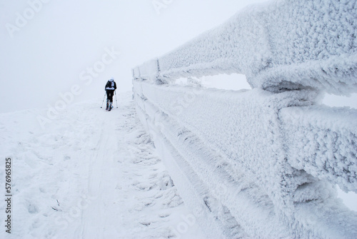 Ski tourer walks along icy fence. photo