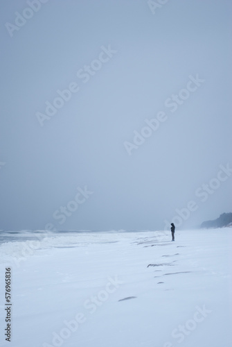 Lonely person standing on snow covered seashore. photo