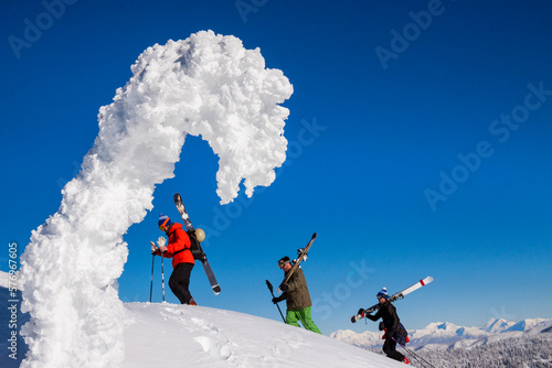 Three Male Skiers Boot Pack Up A Steep Slope Past A Snowghost Near Whitefish, Montana photo