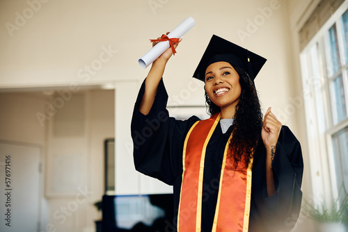 Happy black student holds her diploma while celebrating her graduation at home.