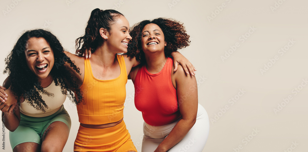 Fun in fitness clothing: Three female friends laughing happily in a sports studio - obrazy, fototapety, plakaty 