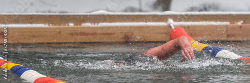 A man swimming in a lake at an ice swimming competition while snow is falling