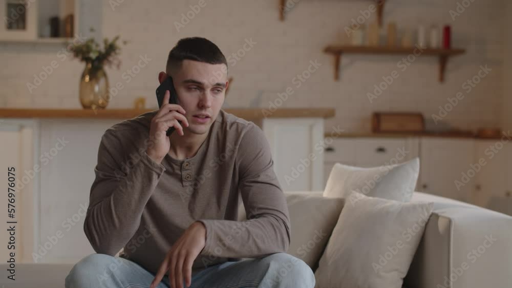 A dark-haired man sitting in a home office is discussing something on the phone and gesturing with his hand. A young businessman discusses the details of a working project with his employee on the A dark-haired man sitting in a home office is discussing something on the phone and gesturing with his hand. A young businessman discusses the details of a working project with his employee on the