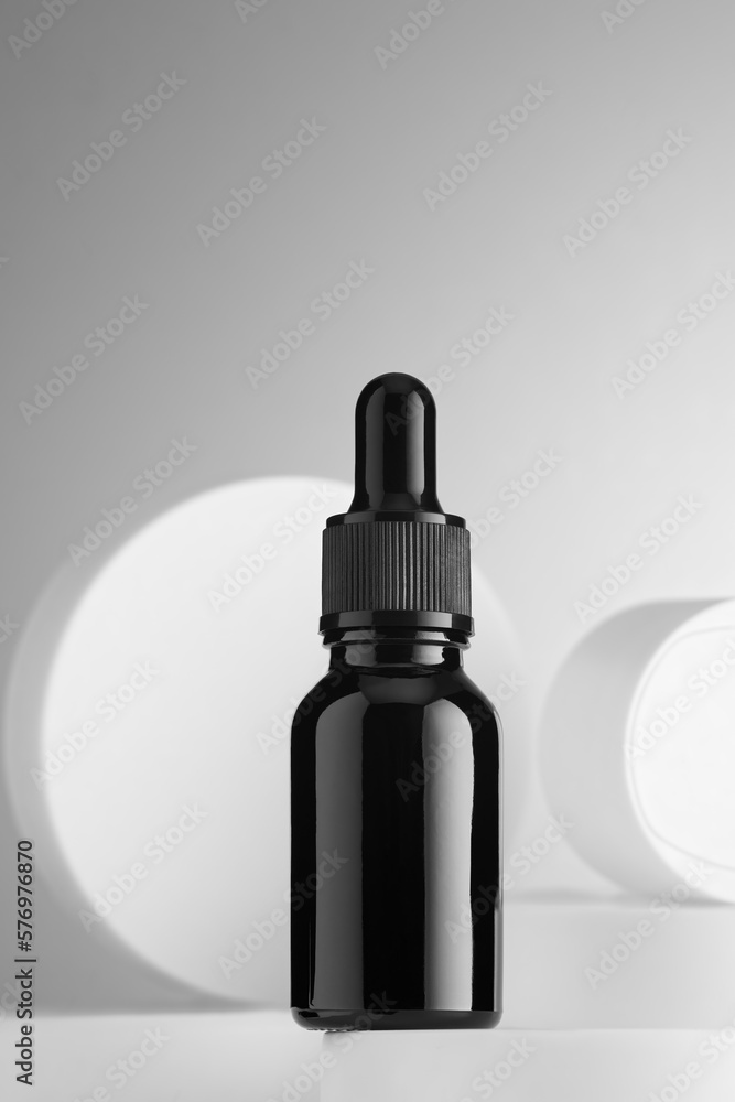 A dark glass bottle with a dropper containing a cosmetic against a background of decorative figures. Copy space. A dark glass bottle with a dropper containing a cosmetic against a background of decorative figures. Copy space.