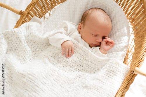 First days of little baby infant sleeping in straw crib wearing white pajamas at home top view. Childhood.