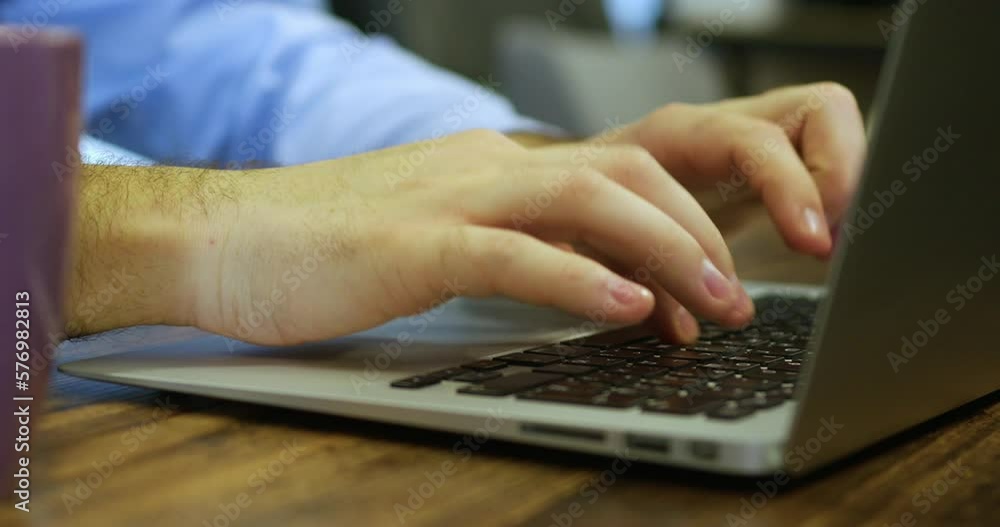 handsome male hands in a blue shirt typing on a laptop keyboard. the boy's fingers on the keys of the keyboard. the manager is typing. close-up handsome male hands in a blue shirt typing on a laptop keyboard. the boy's fingers on the keys of the keyboard. the manager is typing. close-up