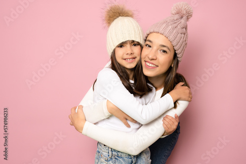 Funny smiling young woman and little kid girl sisters wearing casual t-shirts hugging looking at camera isolated on pink color background studio portrait. Family day concept