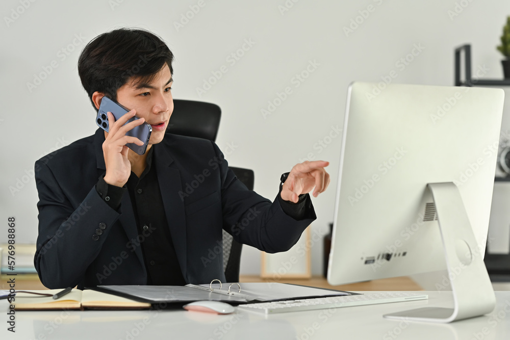 Photo of executive male manager looking at computer screen, discussing project on mobile phone Photo of executive male manager looking at computer screen, discussing project on mobile phone